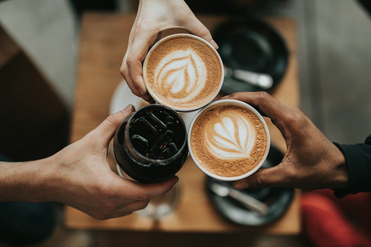 Two lattes with latte art held over a table