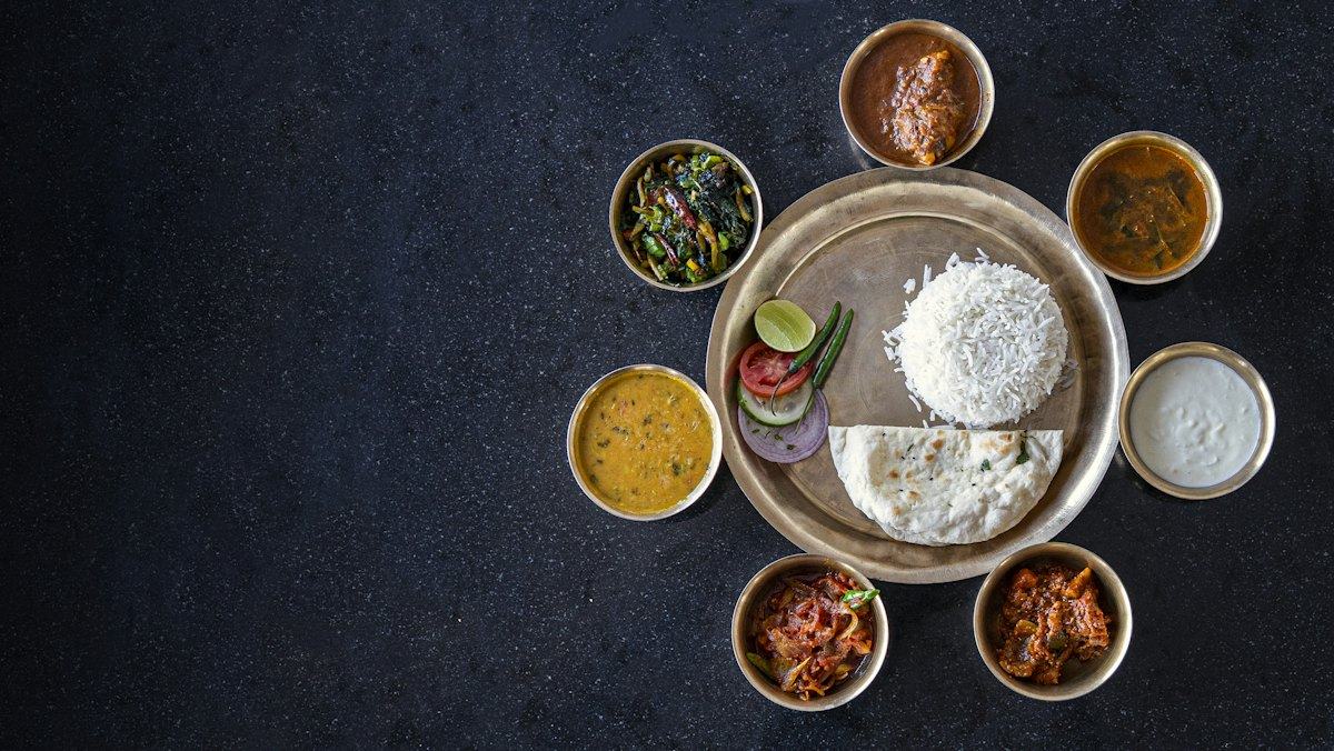 A thali of rice surrounded by small bowls of curries and sides